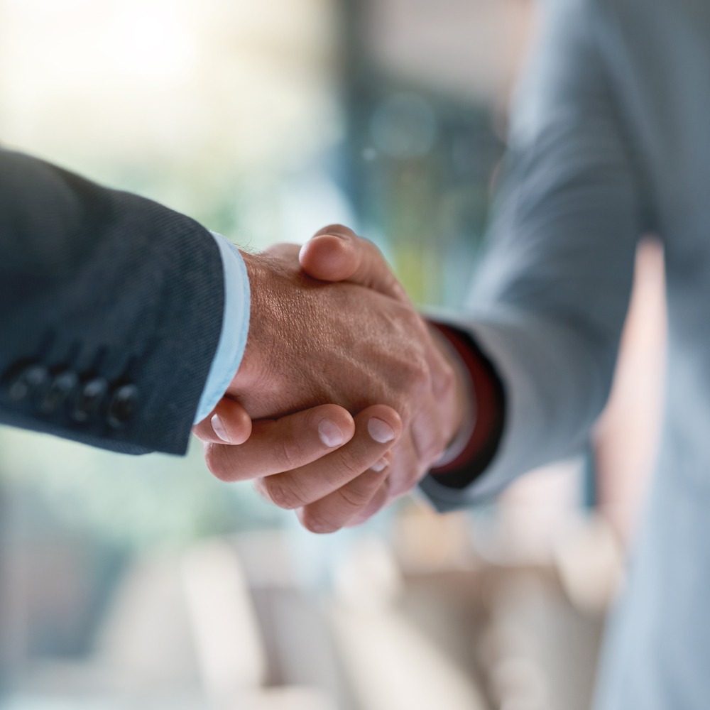 two unrecognizable businessmen shaking hands in an office.